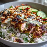 A vibrant Coconut Rice Peanut Bowl garnished with chopped peanuts and lime wedges, showcasing colorful fresh vegetables and succulent meat.  