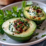 Creamy green avocado deviled eggs garnished with fresh chives and dill for a vibrant spring appetizer.  