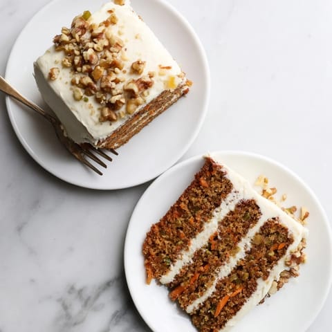 Frosted Carrot Cake slice revealing moist crumb, shredded carrots, and pineapple chunks beside a hot coffee.
