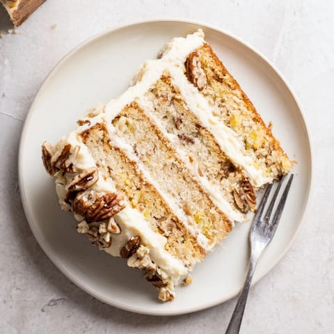A slice of moist Southern Hummingbird Cake showcases its banana and pineapple filling, paired with a hot cup of coffee on a rustic table. 