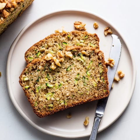 Slices of moist Zucchini Bread with crunchy walnuts, served on a white plate next to a steaming cup of coffee.