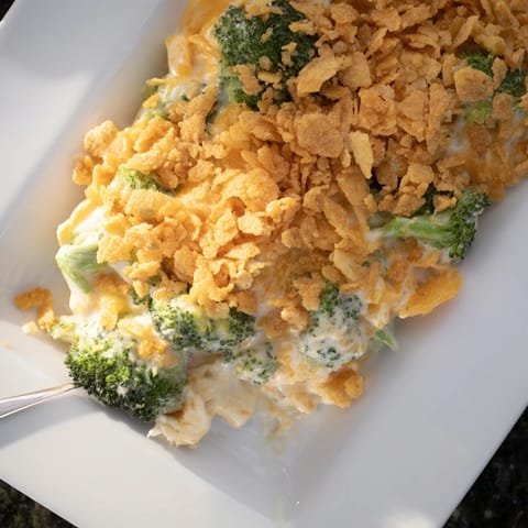 Bright green tender broccoli florets covered in creamy cheese sauce and a golden Ritz cracker crumble in a white baking dish.