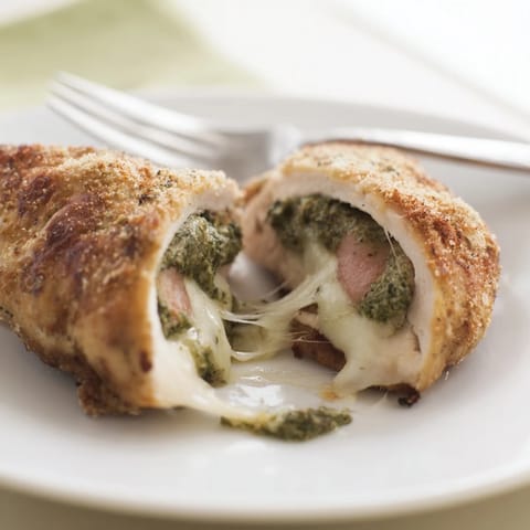 Golden-baked Mozzarella & Pesto Stuffed Chicken breasts oozing melted cheese and bright green pesto, served on a rustic plate.