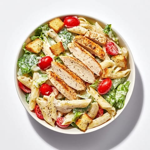 A bowl of Caesar Pasta Chicken Bowl featuring grilled chicken strips, al dente pasta, and crisp romaine tossed in creamy dressing.
