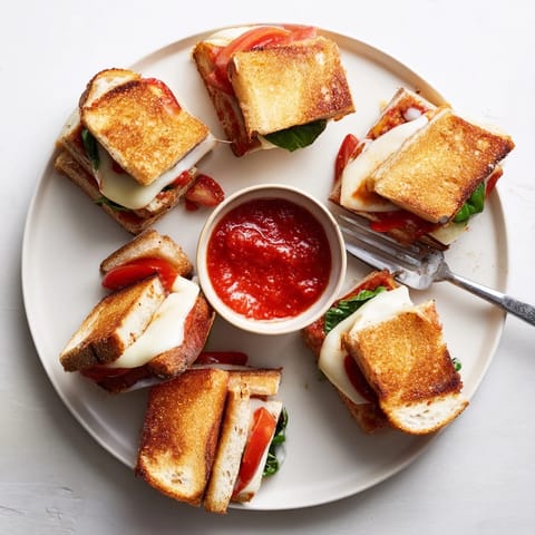 A close-up of Caprese Grilled Cheese Dippers reveals layers of gooey cheese, ripe tomato, and basil between crispy sourdough slices.