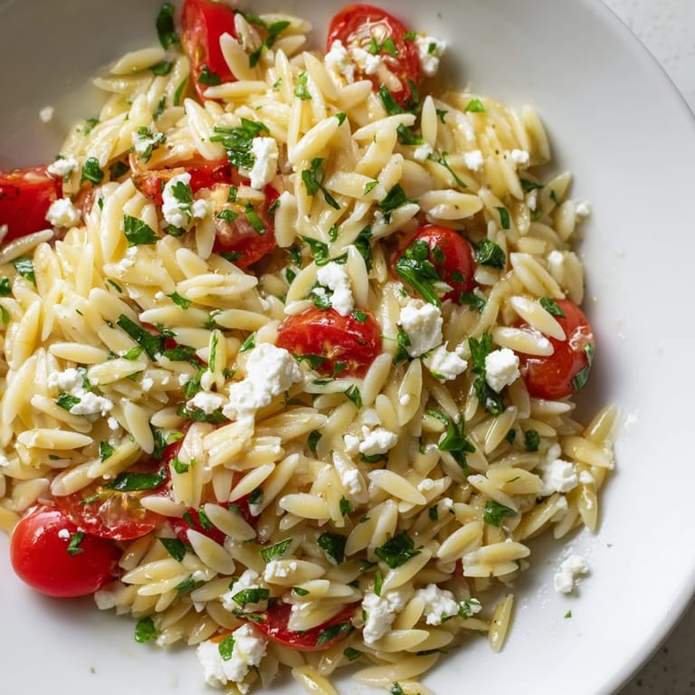 Colorful Greek Orzo Salad with feta crumbles, red onion, and parsley on a wooden table, ready for a picnic side dish.