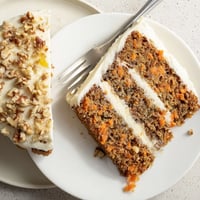 Freshly baked Carrot Cake layers with cream cheese frosting and toasted walnuts on a white ceramic plate.