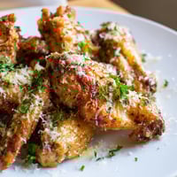 Crispy baked Garlic Parmesan Wings piled high on a platter with fresh parsley and extra cheese.