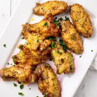 Golden brown Lemon Pepper Wings rest on a wire rack, showcasing crispy skin infused with citrus zest and black pepper.