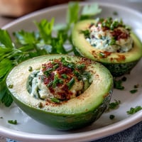 Creamy green avocado deviled eggs garnished with fresh chives and dill for a vibrant spring appetizer.  